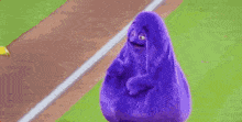 a purple cartoon character standing on a baseball field .