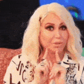 a woman with blonde hair is sitting on a couch with her hands on her face .
