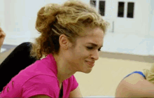 a woman with curly hair wearing a pink shirt