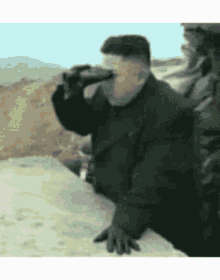a man is drinking from a bottle while looking through binoculars .