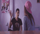 a girl wearing a pink hat is waving at a boy in a black shirt