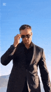 a man in a suit is adjusting his sunglasses .