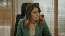 a woman in a green suit is sitting in a chair in front of a window with blinds .