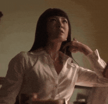 a woman in a white shirt is talking on a phone while sitting at a table .