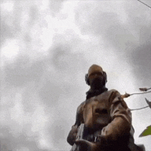 a soldier is standing in front of a cloudy sky holding a rifle .