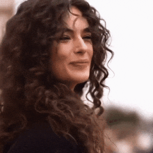 a woman with curly hair is smiling for the camera .