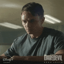 a man in a grey shirt is sitting in front of a poster for daredevil born again