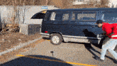 a man in a red jacket pushes a blue van down a road