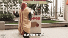 a man in a hot dog costume is dancing in front of a stand that says hatsune miku