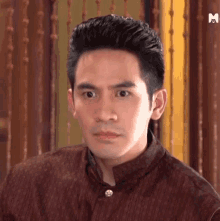 a man in a brown shirt is making a funny face and looking at the camera .