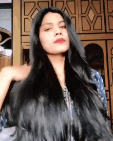 a woman with long black hair is standing in front of a wall