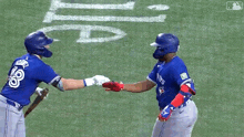 two blue jays baseball players shake hands on the field .
