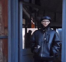 a person wearing glasses and a black jacket stands in a doorway