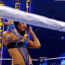 a female wrestler is standing in a wrestling ring holding a rope .