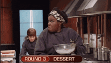 a woman in a kitchen holding a bowl with round 3 dessert written on the sign