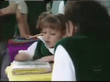 a girl in a green vest sits at a desk with a stack of books