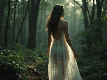 a woman in a sheer white dress walks through a forest
