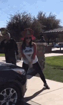 a woman wearing a red hat is standing next to a black car .