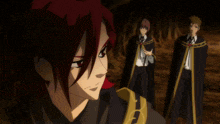 a man in a black cape with a gold embroidery on the hood stands next to two other people