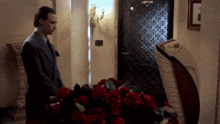 a man in a suit stands in front of a coffin with red roses