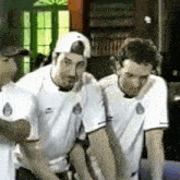 three men are standing next to each other in a room wearing white shirts .