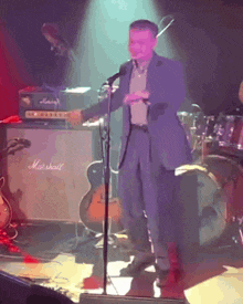 a man in a suit stands in front of a marshall amp