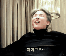 a man wearing a black turtleneck sweater is smiling in front of a window