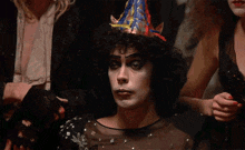 a man with a party hat on his head is sitting with his hands folded .