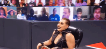a woman is sitting in a chair in front of a screen with a crowd of people .