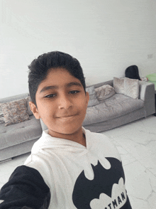 a young boy wearing a batman shirt takes a selfie in front of a couch