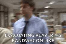 a man in a blue shirt and tie is walking in an office and says evacuating player a 's bandwagon like
