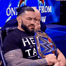 roman reigns is sitting in a chair holding a wrestling belt .