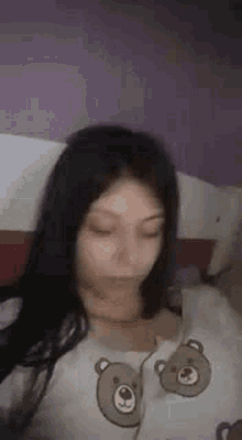 a young woman is laying on a bed wearing a teddy bear shirt .