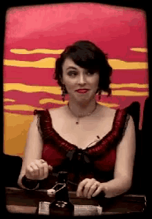 a woman in a red dress is sitting at a table with a bottle of beer in front of her