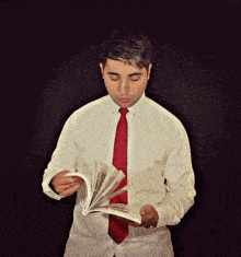 a man in a white shirt and red tie is looking at a book