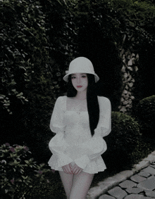 a woman wearing a white hat and a white dress is standing on a path