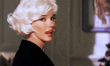 a woman with blonde hair and red lips is looking at something