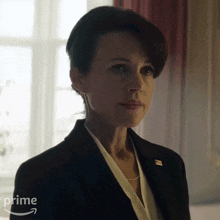 a woman in a suit is standing in front of a window with a prime arrow in the corner