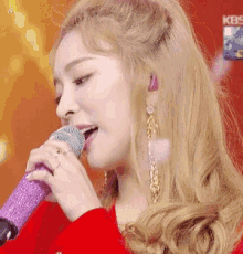 a woman singing into a purple microphone with kbs written on the bottom right