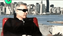 a man wearing sunglasses is sitting in a red chair in front of a city skyline