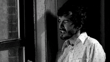 a man with a beard is looking out a window in a black and white photo