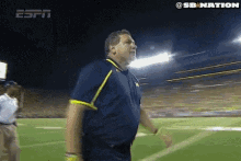 a man in a blue shirt is walking on a football field with espn in the background