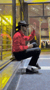 a man in a red shirt and black hat is squatting down in front of a store that says eme
