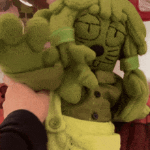 a person is holding a stuffed green monster with a t on its face