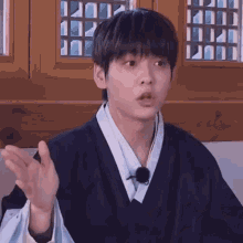 a young man in a traditional korean dress is making a funny face while sitting in front of a window .