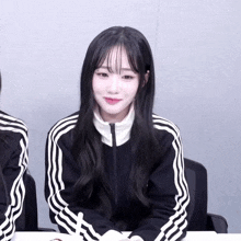 a girl with long black hair wearing a black jacket with white stripes on the sleeves