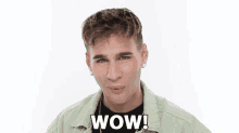 a young man in a green jacket is making a surprised face with the words wow written on his chest .