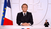 a man in a suit and tie stands in front of a flag