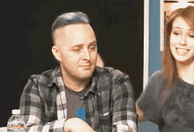 a man in a plaid shirt sits next to a woman with a bottle of water in front of him