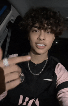 a young man with curly hair is wearing a nike shirt and a necklace
